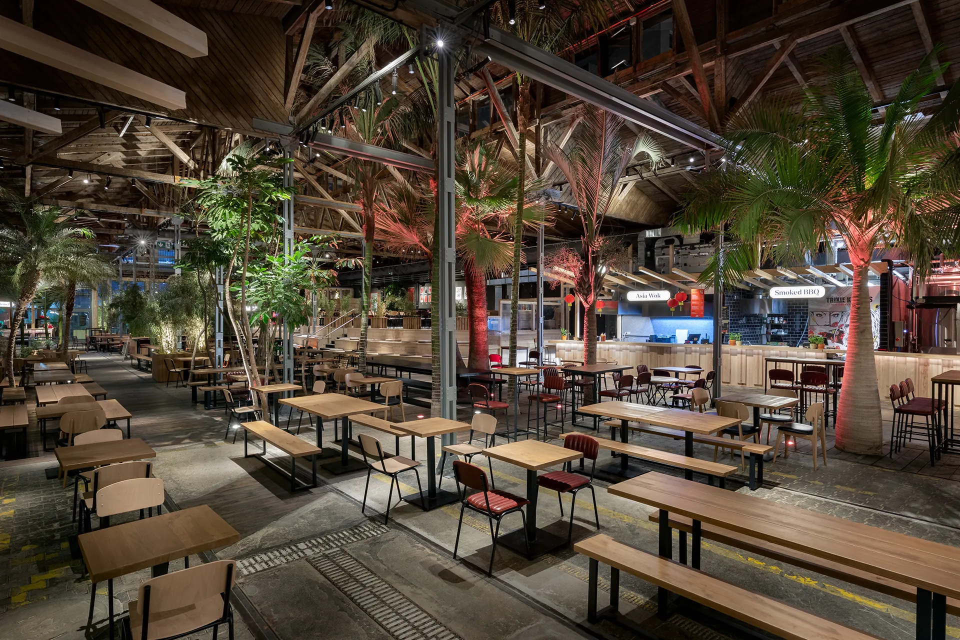 Garden restaurant interior with central tree, layered tables and evening atmosphere.