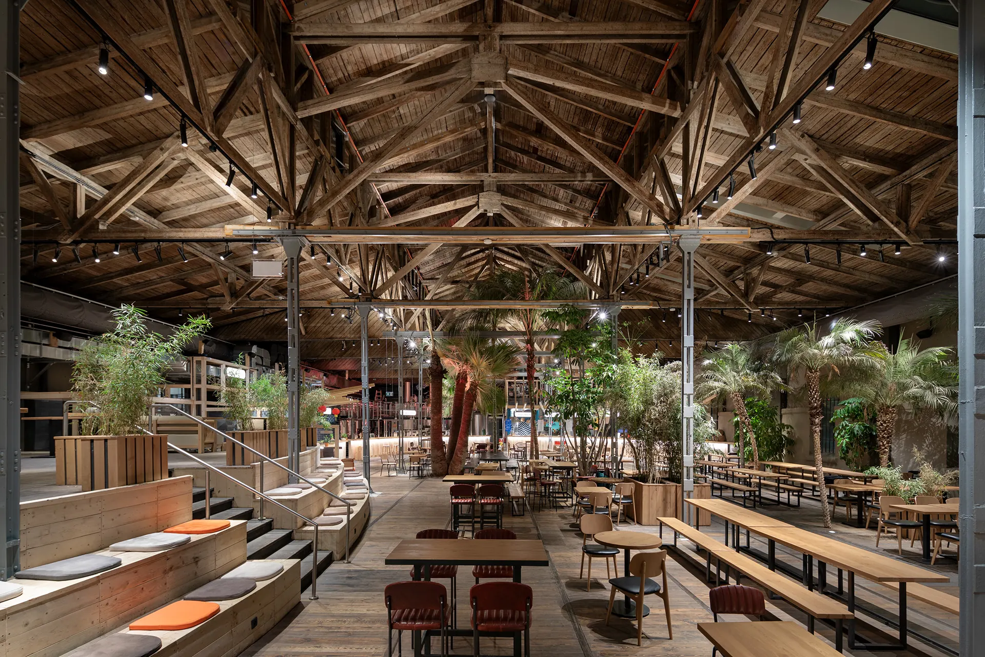 Garden restaurant interior with timber structure, dense planting and warm evening lighting.